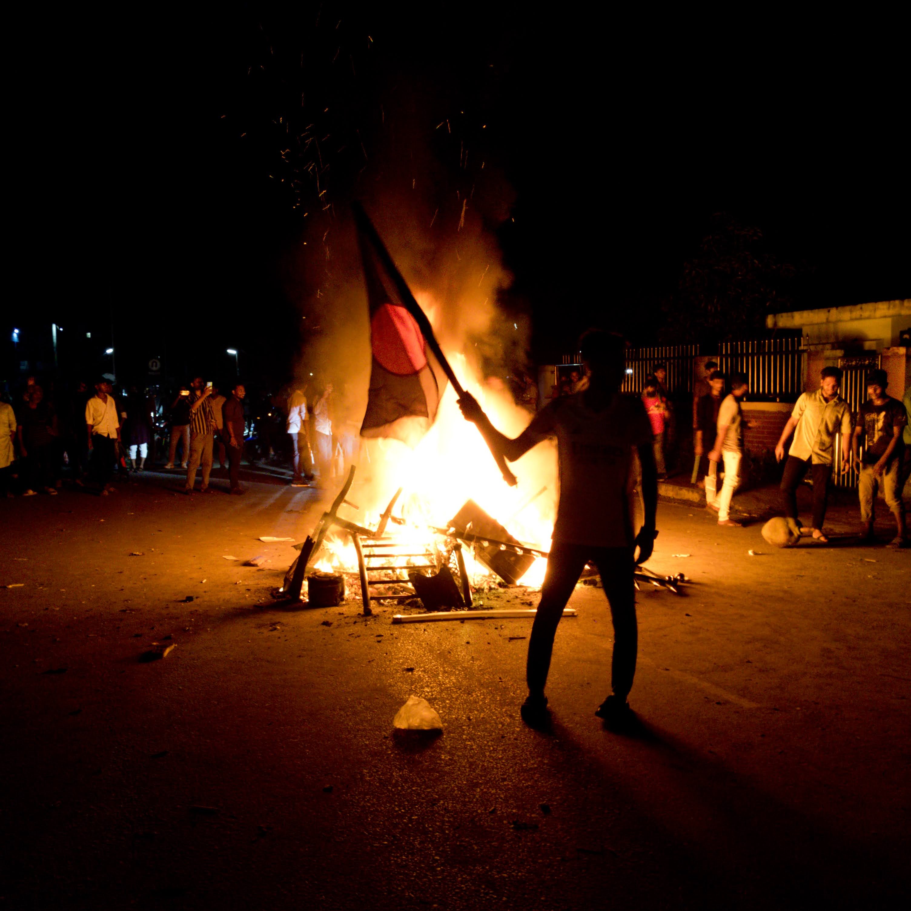 Silhouette of a person holding the Bangladesh flag next to a bonfire at night by miqdad23.
