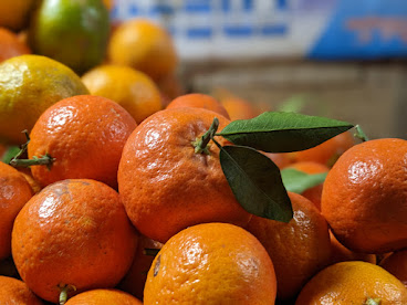 Close-up of fresh ripe oranges with green leaves in a market setting by miqdad23.